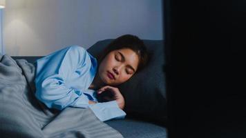 felice giovane donna asiatica addormentata sul divano da sola nel soggiorno mentre guarda film o sport in tv a casa tardi la notte. persona che russa, distanza sociale, quarantena per il concetto di prevenzione del coronavirus. foto