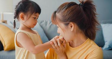 felice allegra famiglia asia mamma e bambina che mangiano ciambelle e si divertono rilassati goditi sul divano nel soggiorno di casa. passare del tempo insieme, distanza sociale, quarantena per il coronavirus. foto