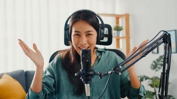 felice ragazza asiatica registra un podcast con cuffie e microfono guarda la telecamera parlare e riposati nella sua stanza. il podcaster femminile crea podcast audio dal suo studio di casa, resta al concetto di casa.