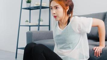 giovane donna coreana in esercizi di abbigliamento sportivo facendo allenamento facendo tuffi tricipiti appoggiata sul divano nel soggiorno di casa. distanza sociale, isolamento durante il virus. esercizi per la parte inferiore del corpo.