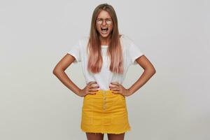 interno foto di giovane stressato lungo dai capelli bionda donna accigliato sua viso mentre urlando ad alta voce, Tenere mani su sua vita mentre in piedi al di sopra di bianca sfondo