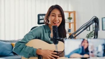 l'influencer di una ragazza asiatica adolescente suona musica per chitarra usa la registrazione del microfono con lo smartphone per il pubblico online ascolta a casa. il podcaster femminile crea podcast audio dal suo studio di casa, resta a casa il concetto.
