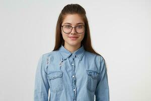 vicino su di simpatico amichevole simpatico giovane ragazza nel occhiali, sta calma, vestito nel un' alla moda denim camicia, isolato su un' bianca sfondo foto