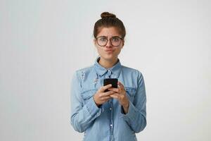 il ragazza sembra con dispiacere a il telecamera, gonfio su sua labbra, deluso, detiene smartphone nel mani, qualcuno fatto non vivere su per sua aspettative, avuto irritato dopo il messaggio, su bianca sfondo foto