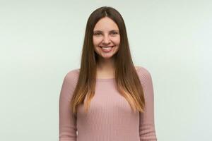 ritratto di giovane donna con lungo capelli fuori uso, sembra lieto, sorridente, vestito nel un' stretto rosa maglia maglione, isolato al di sopra di bianca sfondo foto