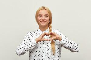 bellissimo giovane ragazza Spettacoli emozione su un' bianca sfondo. ragazza Spettacoli cuore forma gesto. romantico ritratto di tenero affascinante donna foto