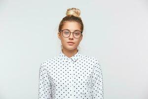 avvicinamento di grave bellissimo giovane donna con ciambella indossa polka punto camicia e bicchieri si sente infelice e sembra per il telecamera isolato al di sopra di bianca sfondo foto