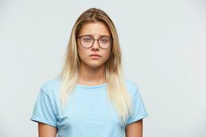 avvicinamento di triste irritato giovane donna con bionda capelli indossa spettacoli e blu t camicia si sente depresso e infelice isolato al di sopra di bianca sfondo foto