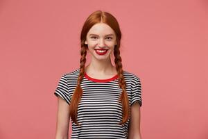 ragazza con Due rosso dai capelli trecce, affascinante trentadue denti Sorridi, Usato rosso rossetto vestito nel nudo maglietta, isolato su un' rosa studio sfondo foto