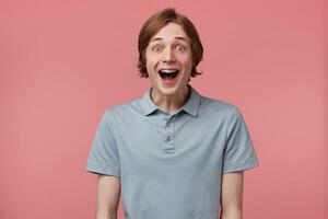 vicino su di stupito eccitato giovane uomo con lungo ordinatamente pettinato capelli e bretelle su denti indossa polo maglietta urlando e si sente contento sorpreso isolato al di sopra di rosa sfondo foto