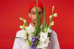 foto di giovane calma buio spellato uomo, indossa nel bianca camicia e rosso cappello, sembra a il telecamera depressione mazzo , sta al di sopra di rosso sfondo.