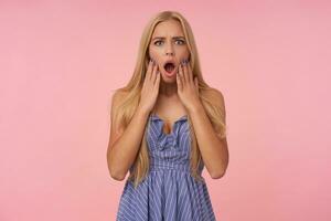 perplesso lungo dai capelli bionda donna con casuale acconciatura guardare a telecamera sorprendentemente con sollevato mani, accigliato per telecamera con largo bocca ha aperto, isolato al di sopra di rosa sfondo foto