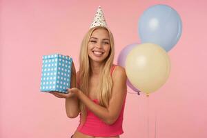 studio foto di contento giovane lungo dai capelli bionda donna con casuale acconciatura gioisce simpatico festa insieme con gli amici, celebra compleanno, in posa al di sopra di rosa sfondo con multicolore aria palloncini