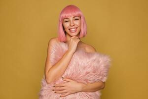 studio foto di attraente giovane positivo rosa dai capelli signora guardare felicemente a telecamera con affascinante Sorridi e dicendo sua mento con sollevato mano, in posa al di sopra di mostarda sfondo con rosa cuscino