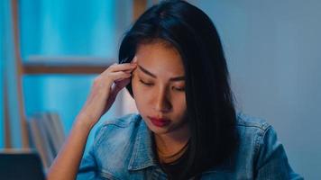 giovane imprenditrice cinese millenaria che lavora a tarda notte stressata con un problema di ricerca del progetto sul laptop nel soggiorno di una casa moderna. concetto di sindrome di burnout professionale di persone asiatiche. foto