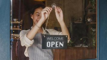 giovane ragazza manager asiatica che cambia un cartello da chiuso a aperto sulla porta del caffè guardando fuori in attesa di clienti dopo il blocco. proprietario piccola impresa, cibo e bevande, affari riaprono concetto. foto