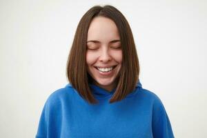 piacevole guardare giovane allegro Marrone dai capelli donna con peso taglio di capelli conservazione sua occhi chiuso mentre sorridente felicemente, vestito nel sportivo Abiti mentre in posa al di sopra di bianca sfondo foto