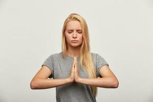 vicino su di Meditare bionda, si concentra su qualche cosa, praticante respirazione yoga esercizio, Tenere sua mani nel yoga gesto, occhi Chiuso, cerca per ottenere sbarazzarsi di fatica, al di sopra di bianca sfondo foto