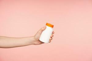 studio foto di giovane femminile mano con nudo manicure conservazione bottiglia con pillole nel esso mentre essere isolato al di sopra di rosa sfondo. assistenza sanitaria e bellezza concetto