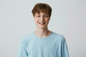 adolescente con corto capelli e bretelle su denti sembra telecamera, indossa blu maglietta, si sente contento lieto, sorridente isolato al di sopra di bianca sfondo foto