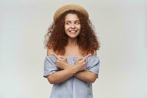 adolescenziale ragazza, contento guardare donna con Riccio Zenzero capelli. indossare a strisce spalle scoperte camicetta e cappello. Guardando per il sinistra a copia spazio e puntamento tutti e due lati, isolato al di sopra di bianca sfondo foto