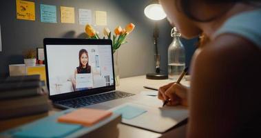 giovane asia teen girl studente lezione di apprendimento a distanza con insegnante online e studio sullo schermo del laptop nel soggiorno a casa notte. a distanza, distanziamento sociale, quarantena per la prevenzione del virus corona. foto