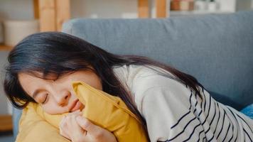 la giovane donna asiatica si sdraia su un comodo divano nel soggiorno, dorme dopo una dura giornata di lavoro e si sente male e male, la femmina stanca si addormenta sul divano a casa, fa un pisolino o sogna ad occhi aperti, concetto di fatica.