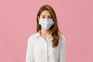 giovane ragazza asiatica che indossa una maschera medica con vestiti in abiti casual e guarda la macchina fotografica isolata su sfondo rosa. autoisolamento, distanziamento sociale, quarantena per la prevenzione del virus corona.