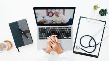 vista dall'alto della giovane dottoressa asiatica in uniforme medica con stetoscopio utilizzando il computer portatile che parla in videoconferenza con il paziente alla scrivania in clinica o ospedale. concetto di consulenza e terapia. foto