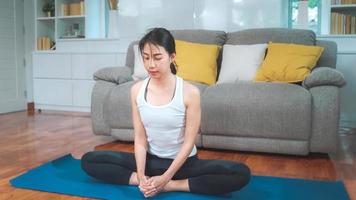 giovane donna asiatica che pratica yoga nel soggiorno. bella femmina attraente che risolve per sano a casa. concetto di esercizio della donna di stile di vita.
