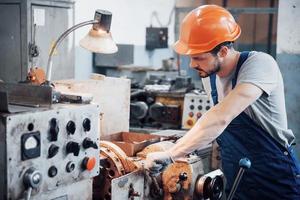 ritratto di un giovane lavoratore con un elmetto in un grande impianto di lavorazione dei metalli. l'ingegnere serve le macchine e produce parti per apparecchiature a gas foto