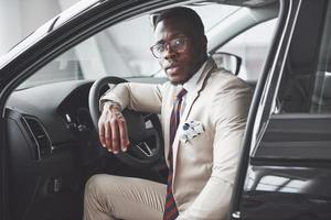 elegante uomo d'affari nero seduto al volante della nuova auto di lusso. ricco uomo afroamericano foto