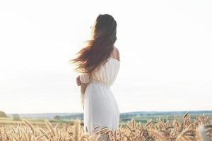 bella ragazza in abito bianco che corre sul campo di grano autunnale all'ora del tramonto foto