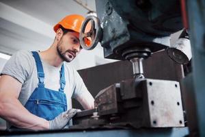 ritratto di un giovane lavoratore con un elmetto in una grande fabbrica di riciclaggio dei rifiuti. l'ingegnere controlla il lavoro di macchine e altre attrezzature foto