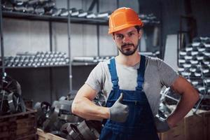 ritratto di un giovane lavoratore con un elmetto in un grande impianto di lavorazione dei metalli. addetto al magazzino dei prodotti finiti foto