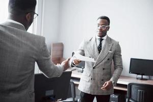 discutere di un progetto. due uomini d'affari neri in abiti da cerimonia che discutono di qualcosa mentre uno di loro indica un foglio foto