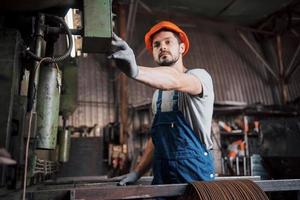 ritratto di un giovane lavoratore con un elmetto in una grande fabbrica di riciclaggio dei rifiuti. l'ingegnere controlla il lavoro di macchine e altre attrezzature foto