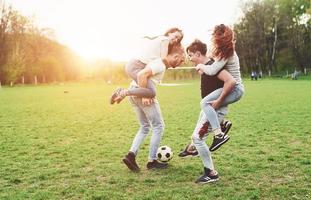 un gruppo di amici in abbigliamento casual gioca a calcio all'aria aperta. le persone si divertono e si divertono. riposo attivo e tramonto panoramico. foto