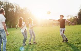 un gruppo di amici in abbigliamento casual gioca a calcio all'aria aperta. le persone si divertono e si divertono. riposo attivo e tramonto panoramico.