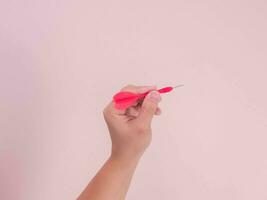 femmina mano Tenere dardo isolato su rosa sfondo. avvicinamento mano ottenere pronto per gettare un' plastica dardo mancia. foto
