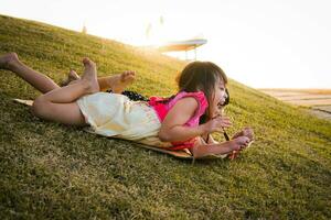 contento sorelle giocando a il parco scivoli giù a partire dal il erboso collina seduta su un' cartone scatola. contento bambini giocando all'aperto nel estate. famiglia la spesa tempo insieme su vacanza. foto