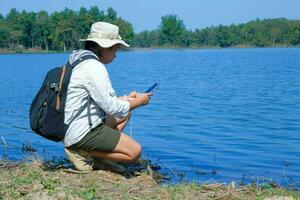 femmina ambientalista utilizzando mobile Telefono per disco analisi di agenti patogeni nel naturale acque. acqua e ecologia concetto foto