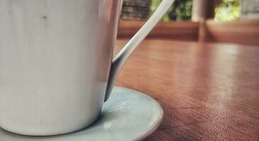 vicino su Visualizza di un' bianca caffè tazza posto su un' Marrone di legno tavolo foto