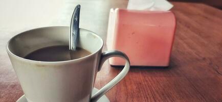 caldo caffè nel un' bianca caffè tazza è posto su un' di legno tavolo nel un' caldo e leggero atmosfera foto