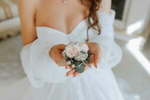 il quello dello sposo boutonniere è disposte a partire dal rosa fiori nel il mani di il sposa con un' francese manicure nel il meraviglioso naturale leggero a partire dal il finestra foto