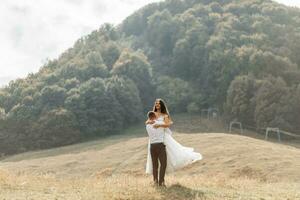 nozze coppia, passeggiate nel il montagne. foto di un' largo Piano. gratuito spazio. il sposo gira il sposa nel il suo braccia, il della sposa vestito si sviluppa nel il vento.