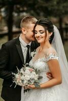 ritratto di il sposa e sposo nel il parco, il sposa e sposo siamo abbracciare e teneramente baciare. nozze camminare nel il parco foto