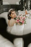 ritratto di un' giovane ragazza a partire dal il Indietro, con bellissimo capelli e trucco nel un' lussuoso nozze vestito su il passaggi di un' ristorante vicino rosa fiori. verticale foto. foto