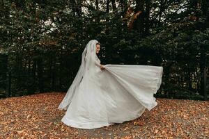 ritratto di il sposa. il sposa gira felicemente, Tenere sua vestito nel sua mani. lungo treno di il vestire. voluminoso velo. cristallo gioielleria foto