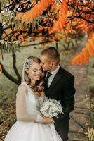 ritagliata ritratto di un' coppia nel amore nel un autunno parco. un' bionda sposa nel un' nozze vestito con maniche e un' mazzo di fiori nel sua mani. il sposo è nel un' classico nero completo da uomo, bianca camicia e cravatta foto